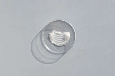 White creamy texture in a Petri dish on a gray background. Concept of cosmetics laboratory researches. Smear of skincare cosmetics product. Wellness and beauty conceptの写真素材
