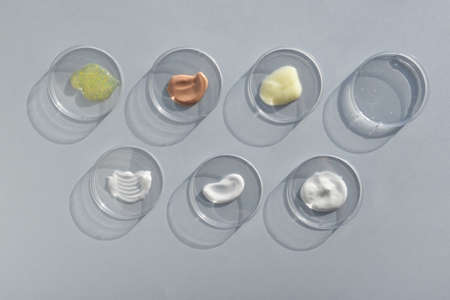 Multicolored texture of cream, scrub, serum and oil in Petri dishes on a gray background. Concept of cosmetics laboratory researches. Smear of skincare cosmetics product. wellness and beauty conceptの写真素材