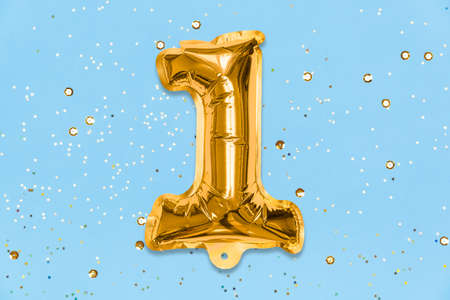 The number of the balloon made of golden foil, the number one on a blue background with sequins. Birthday greeting card with inscription 1. Top view. Numerical digit, Celebration event, template.の写真素材