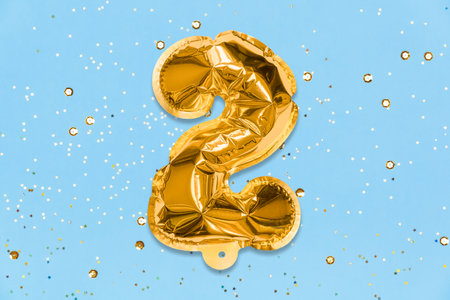 The number of the balloon made of golden foil, the number two on a blue background with sequins. Birthday greeting card with inscription 2. Top view. Numerical digit, Celebration event, template.の写真素材