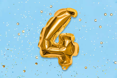The number of the balloon made of golden foil, the number four on a blue background with sequins. Birthday greeting card with inscription 4. Top view. Numerical digit, Celebration event, template.の写真素材