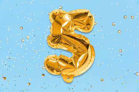 The number of the balloon made of golden foil, the number five on a blue background with sequins. Birthday greeting card with inscription 5. Top view. Numerical digit, Celebration event, template.の写真素材