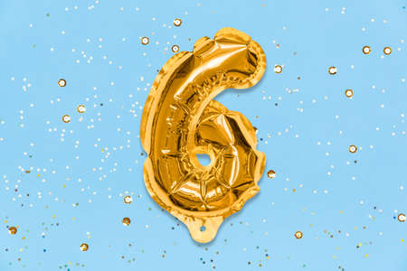 The number of the balloon made of golden foil, the number six on a blue background with sequins. Birthday greeting card with inscription 6. Top view. Numerical digit, Celebration event, template.の写真素材