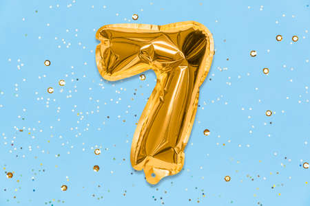 The number of the balloon made of golden foil, the number seven on a blue background with sequins. Birthday greeting card with inscription 7. Top view. Numerical digit, Celebration event, template.の写真素材