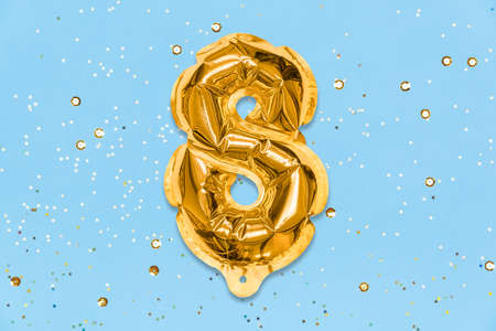 The number of the balloon made of golden foil, the number eight on a blue background with sequins. Birthday greeting card with inscription 8. Top view. Numerical digit, Celebration event, template.の写真素材