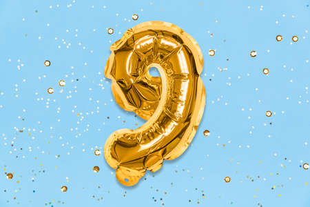 The number of the balloon made of golden foil, the number nine on a blue background with sequins. Birthday greeting card with inscription 9. Top view. Numerical digit, Celebration event, template.の写真素材