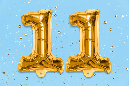 The number of the balloon made of golden foil, the number eleven on a blue background with sequins. Birthday greeting card with inscription 11. Top view. Numerical digit, Celebration event, template.の写真素材