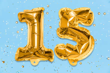 The number of the balloon made of golden foil, the number fifteen on a blue background with sequins. Birthday greeting card with inscription 15. Anniversary concept. Celebration event.の写真素材