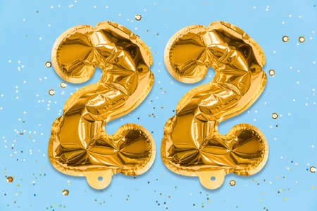The number of the balloon made of golden foil, the number twenty two on a blue background with sequins. Birthday greeting card with inscription 22. Numerical digit, Celebration event, template.の写真素材