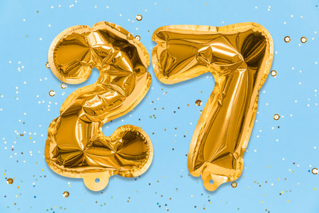 The number of the balloon made of golden foil, the number twenty-seven on a blue background with sequins. Birthday greeting card with inscription 27. Numerical digit, Celebration event, template.の写真素材