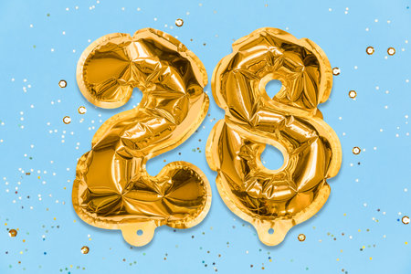 The number of the balloon made of golden foil, the number twenty-eight on a blue background with sequins. Birthday greeting card with inscription 28. Numerical digit, Celebration event, template.の写真素材