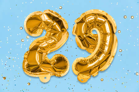 The number of the balloon made of golden foil, the number twenty-nine on a blue background with sequins. Birthday greeting card with inscription 29. Numerical digit, Celebration event, template.の写真素材