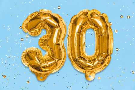 The number of the balloon made of golden foil, the number thirty on a blue background with sequins. Birthday greeting card with inscription 30. Anniversary concept. Numerical digit, Celebration event.の写真素材
