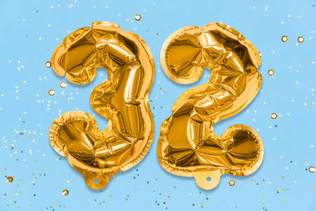 The number of the balloon made of golden foil, the number thirty two on a blue background with sequins. Birthday greeting card with inscription 32. Numerical digit, Celebration event, template.の写真素材