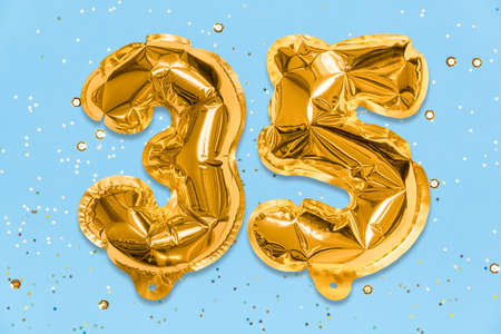 The number of the balloon made of golden foil, the number thirty-five on a blue background with sequins. Birthday greeting card with inscription 35. Anniversary concept. celebration event.の写真素材