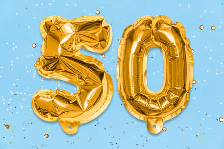 The number of the balloon made of golden foil, the number fifty on a blue background with sequins. Birthday greeting card with inscription 50. Anniversary concept. Numerical digit. Celebration event.の写真素材