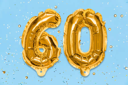 The number of the balloon made of golden foil, the number sixty on a blue background with sequins. Birthday greeting card with inscription 60. Anniversary concept. Numerical digit. celebration event.の写真素材