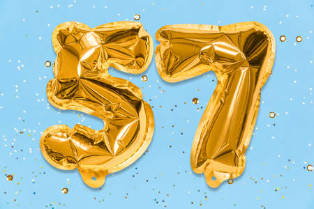 The number of the balloon made of golden foil, the number fifty-seven on a blue background with sequins. Birthday greeting card with inscription 57. Numerical digit. Celebration event template.の写真素材