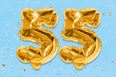 The number of the balloon made of golden foil, the number fifty-five on a blue background with sequins. Birthday greeting card with inscription 55. Anniversary concept. celebration event.の写真素材