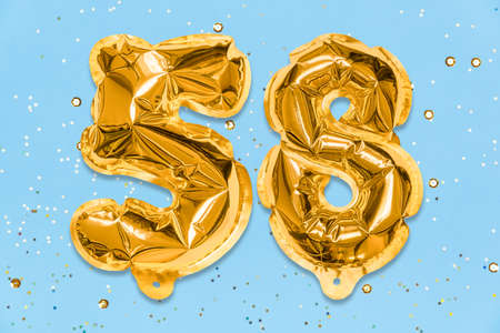 The number of the balloon made of golden foil, the number fifty-eight on a blue background with sequins. Birthday greeting card with inscription 58. Numerical digit. Celebration event template.の写真素材