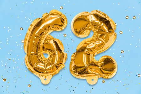 The number of the balloon made of golden foil, the number sixty-two on a blue background with sequins. Birthday greeting card with inscription 62. Numerical digit. Celebration event template.の写真素材