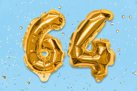 The number of the balloon made of golden foil, the number sixty-four on a blue background with sequins. Birthday greeting card with inscription 64. Numerical digit. Celebration event template.の写真素材