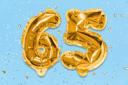 The number of the balloon made of golden foil, the number sixty-five on a blue background with sequins. Birthday greeting card with inscription 65. Anniversary concept. celebration event.の写真素材