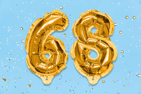 The number of the balloon made of golden foil, the number sixty-eight on a blue background with sequins. Birthday greeting card with inscription 68. Numerical digit. Celebration event template.の写真素材