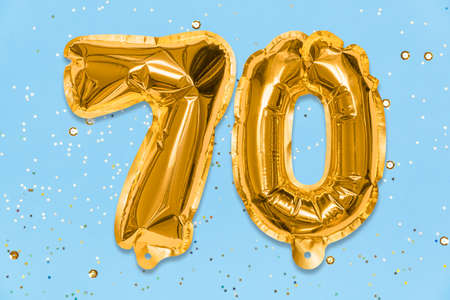 The number of the balloon made of golden foil, the number seventy on a blue background with sequins. Birthday greeting card with inscription 70. Anniversary concept. celebration event.の写真素材
