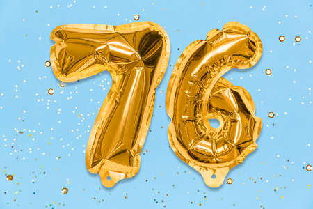 The number of the balloon made of golden foil, the number seventy-six on a blue background with sequins. Birthday greeting card with inscription 76. Numerical digit. Celebration event, template.の写真素材