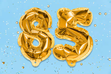 The number of the balloon made of golden foil, the number eighty-five on a blue background with sequins. Birthday greeting card with inscription 85. Anniversary concept. celebration event.の写真素材