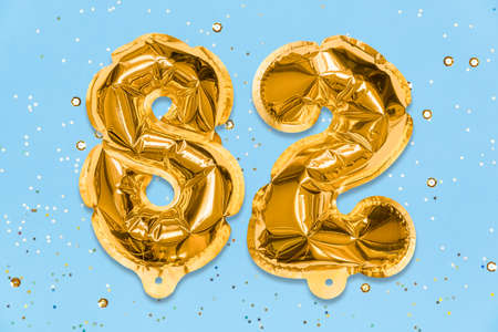 The number of the balloon made of golden foil, the number eighty-two on a blue background with sequins. Birthday greeting card with inscription 82. Numerical digit. Celebration event template.の写真素材
