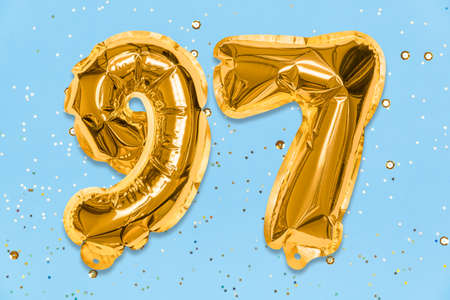 The number of the balloon made of golden foil, the number ninety-seven on a blue background with sequins. Birthday greeting card with inscription 97. Numerical digit. Celebration event template.の写真素材