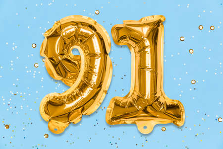 The number of the balloon made of golden foil, the number ninety-one on a blue background with sequins. Birthday greeting card with inscription 91. Numerical digit. Celebration event template.の写真素材
