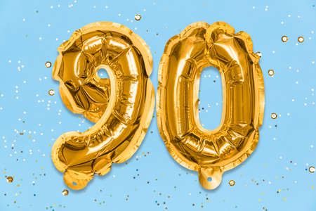 The number of the balloon made of golden foil, the number ninety on a blue background with sequins. Birthday greeting card with inscription 90. Anniversary concept. Celebration event template.の写真素材