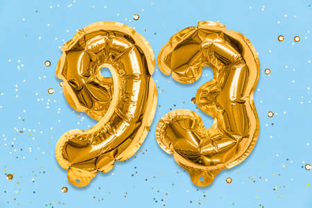 The number of the balloon made of golden foil, the number ninety-three on a blue background with sequins. Birthday greeting card with inscription 93. Numerical digit. Celebration event template.の写真素材
