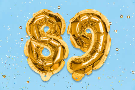 The number of the balloon made of golden foil, the number eighty-nine on a blue background with sequins. Birthday greeting card with inscription 89. Numerical digit. Celebration event template.の写真素材