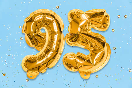 The number of the balloon made of golden foil, the number ninety-five on a blue background with sequins. Birthday greeting card with inscription 95. Anniversary concept. celebration event.の写真素材