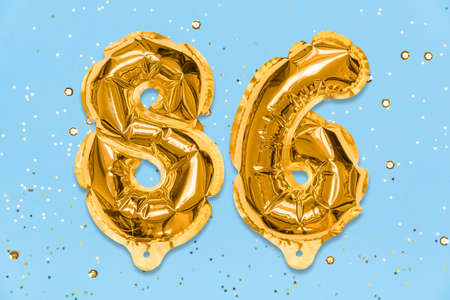The number of the balloon made of golden foil, the number eighty-six on a blue background with sequins. Birthday greeting card with inscription 86. Numerical digit. Celebration event template.の写真素材