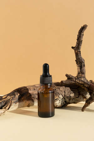 Bottle of dark amber glass with hyaluronic acid or face serum near dry branch on a beige background. Concept natural cosmetics with organic components. Copy space for your designs. front view.の写真素材