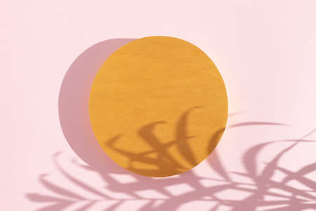 Abstract minimal scene of a geometrical shape. A cylindrical golden podium on a pink background with a shadow of tropical palm leaves. Scene to show cosmetic products. Show case, display case.の写真素材