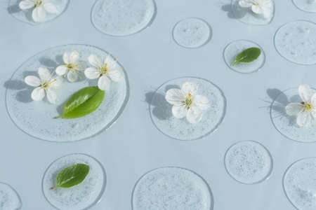 Drops of transparent cosmetic gel or serum with white flowers and green leaves on a pastel blue background. The concept of natural cosmetics. top view. selective focus.の写真素材