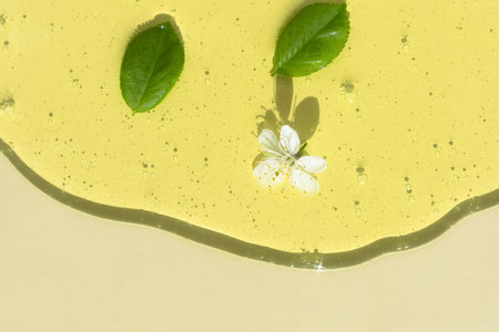 Transparent cosmetic gel or serum of yellow color with a white flower and green leaves on a light background. The concept of natural cosmetics. top view. selective focus.の写真素材