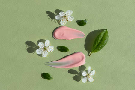 Smears of pink cream with white flowers and green leaves on a green background. The texture of a cosmetic skin care product. The concept of natural cosmetics. top view.の写真素材
