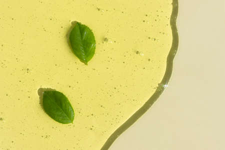 Transparent cosmetic gel or serum of yellow color with green leaves on a light beige background. The concept of natural cosmetics. top view.の写真素材