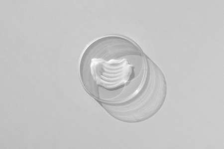 White creamy texture in a Petri dish on a gray background. Concept of cosmetics laboratory researches. Smear of skincare cosmetics product. wellness and beauty concept.の写真素材