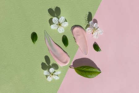 Smears of pink cream with white flowers and green leaves on a green and pink background. The texture of a cosmetic skin care product. The concept of natural cosmetics. top view.の写真素材