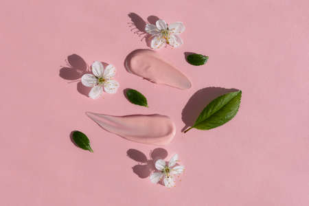 Smears of pink cream with white flowers and green leaves on a pink background. The texture of a cosmetic skin care product. The concept of natural cosmetics. top view.の写真素材