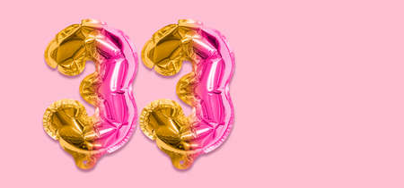 Rainbow foil balloon number, digit thirty three on a pink background. Birthday greeting card with inscription 33. Top view. Numerical digit. Celebration event template. Banner.の写真素材
