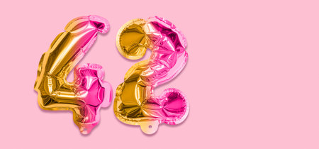Rainbow foil balloon number, digit forty two on a pink background. Birthday greeting card with inscription 42. Top view. Numerical digit. Celebration event template. Banner.の写真素材